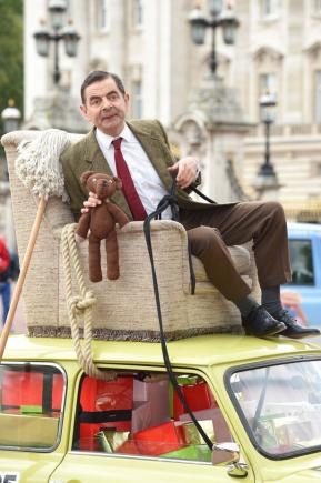 25 de ani de Mr Bean. Actorul a defilat prin fața Palatului Buckingham pe un fotoliu legat de capota unei mașini, cu un mop în mână (VIDEO)